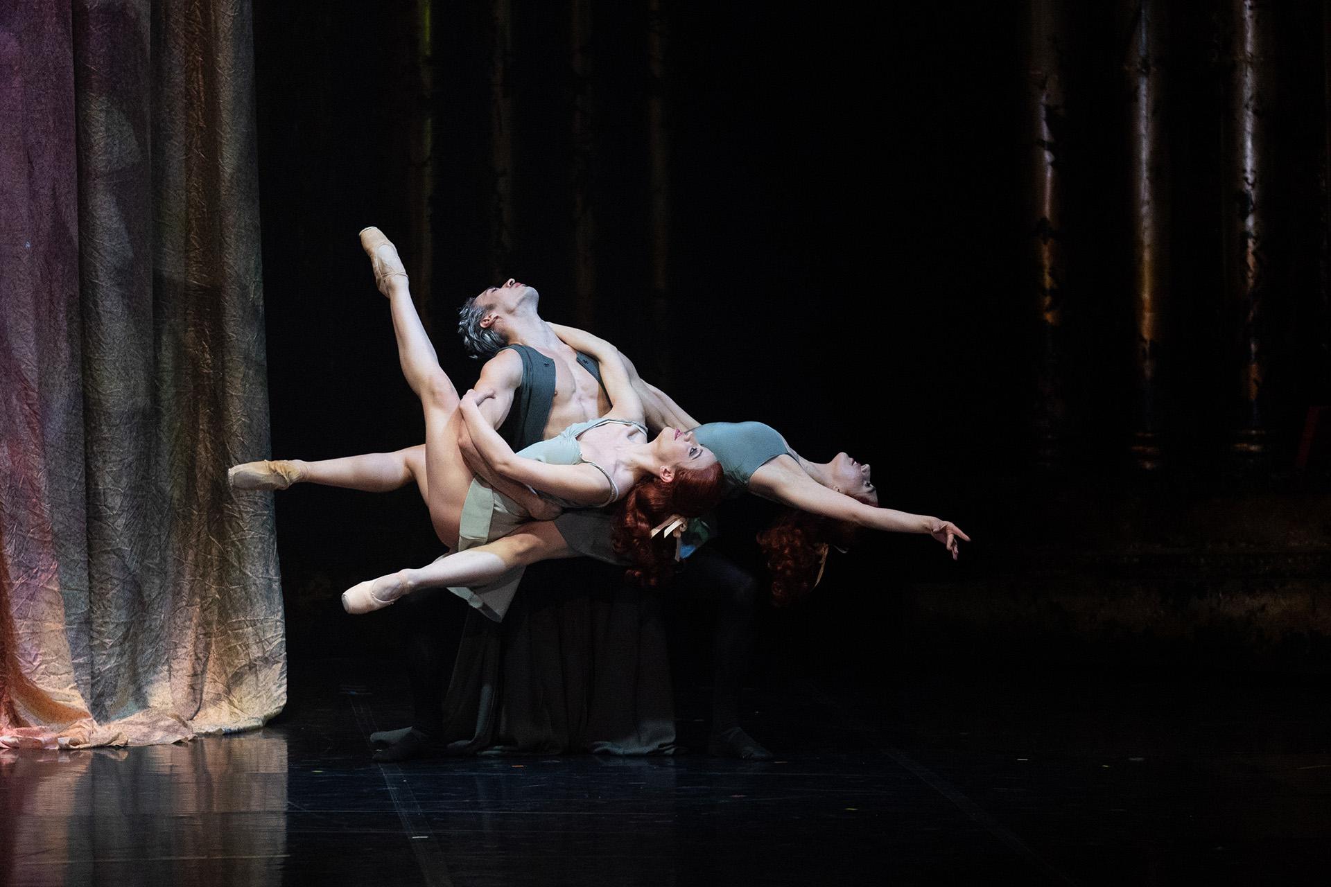 Dancer holding two other dancers off the ground, them leaning back balanced on his hips
