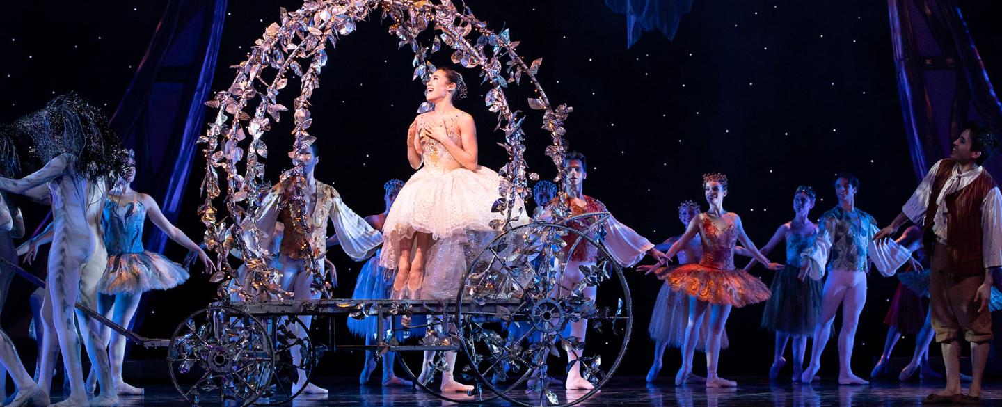 Dressing white, a dancer rides an open, decorated carriage surrounded by onlookers